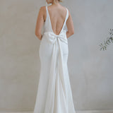 Woman wearing a Crepe Fit and Flare Wedding Dress with a bow detail in a minimalistic setting.