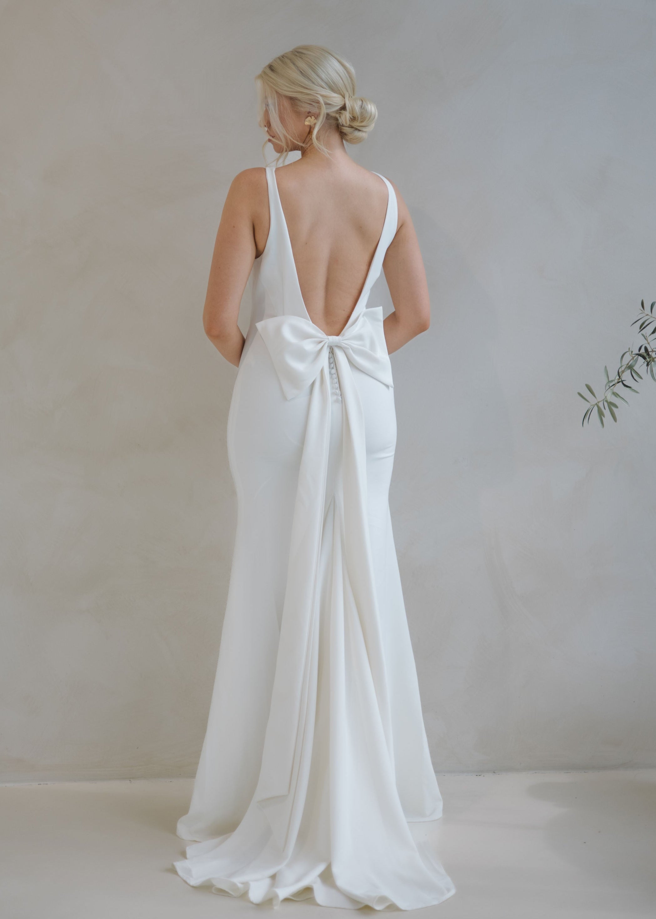 Woman wearing a Crepe Fit and Flare Wedding Dress with a bow detail in a minimalistic setting.