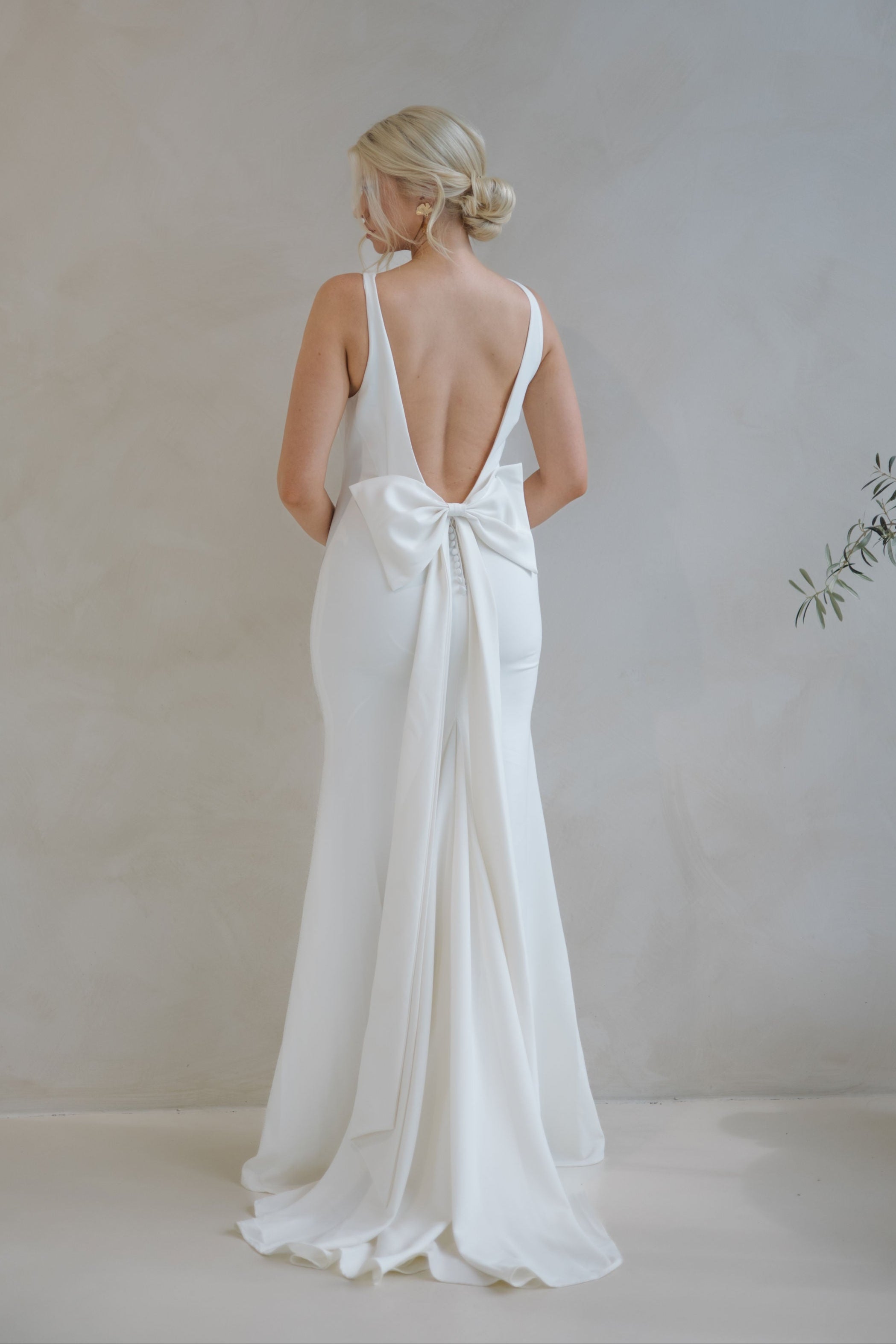 Woman wearing a Crepe Fit and Flare Wedding Dress with a bow detail in a minimalistic setting.