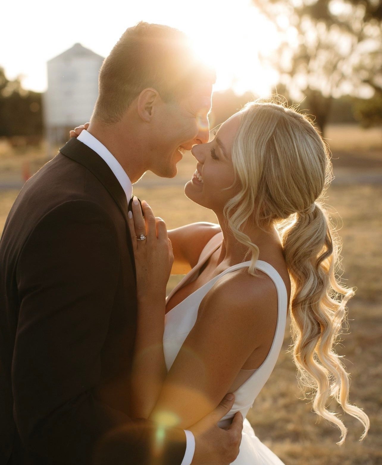 Couple embracing with a warm glow, likely from the sun, in an outdoor setting.