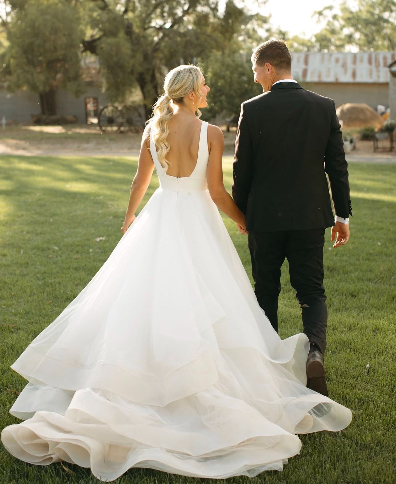 Couple in wedding attire walking on grass with trees in the background