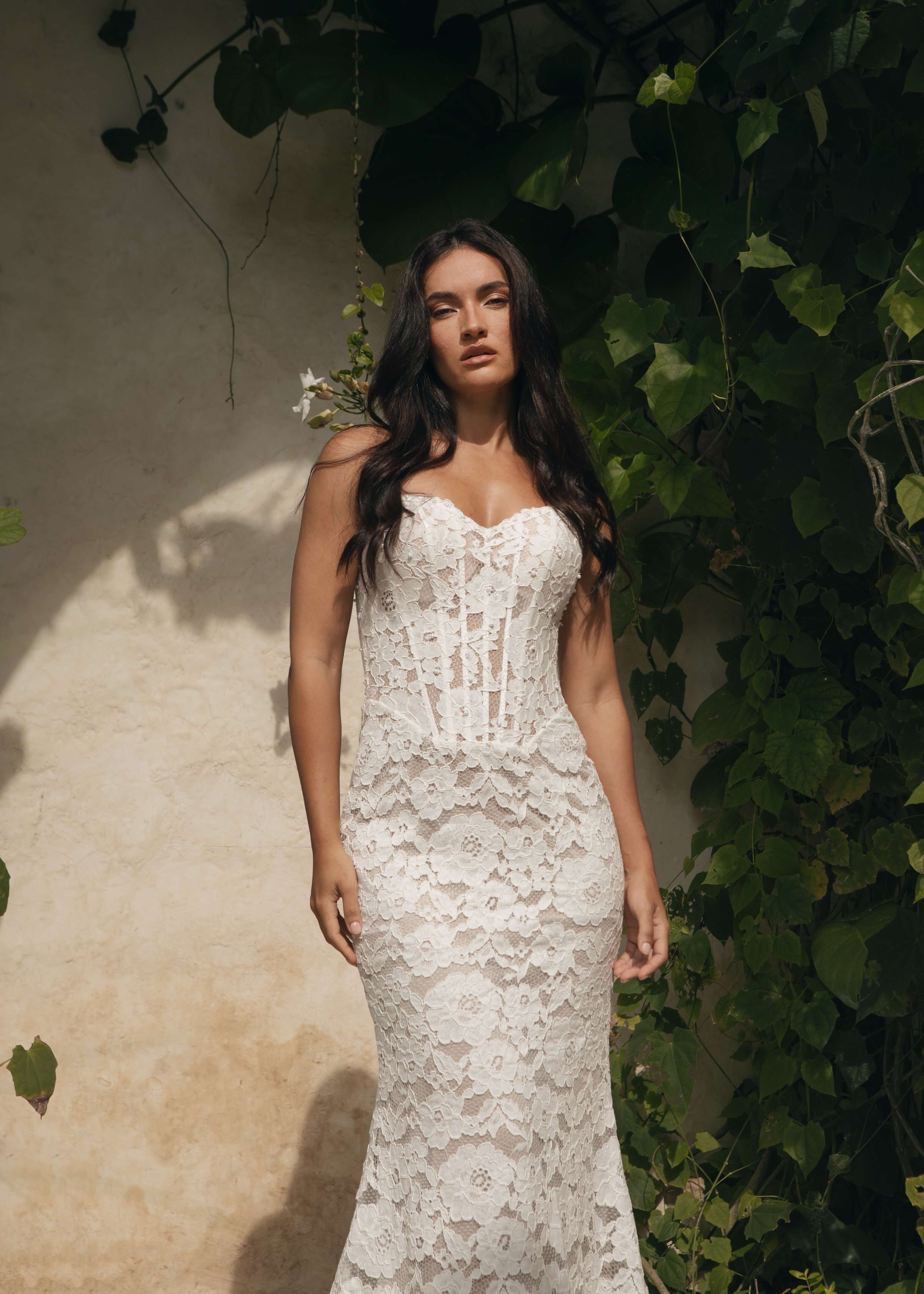 Woman wearing a Lace A-Line Wedding Dress standing against a textured wall with greenery.