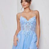 Woman wearing a light blue evening gown with lace details against a plain background