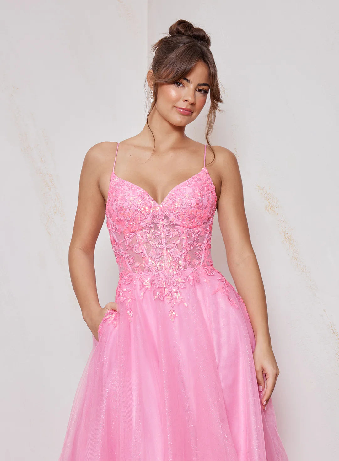 Woman wearing a pink evening gown with floral lace details on a light background