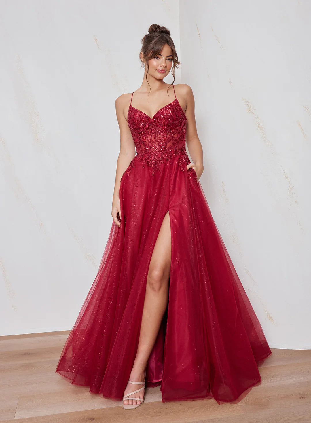 Woman wearing a red evening gown with a slit on a plain background