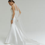 Woman wearing a dropped waist Mikado fitted wedding dress on a plain background