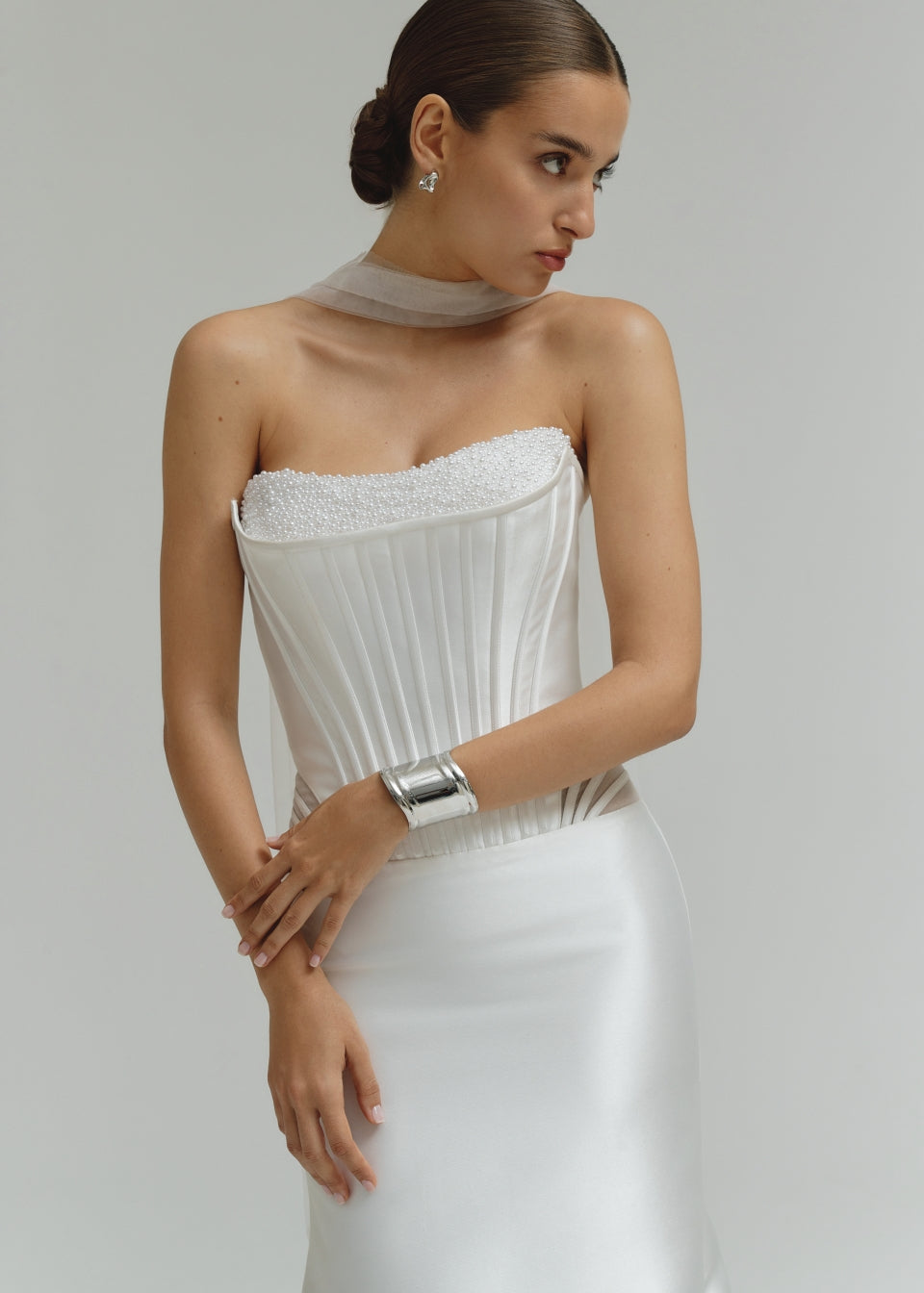 Woman wearing a dropped waist Mikado fitted wedding dress with a textured bodice on a plain background