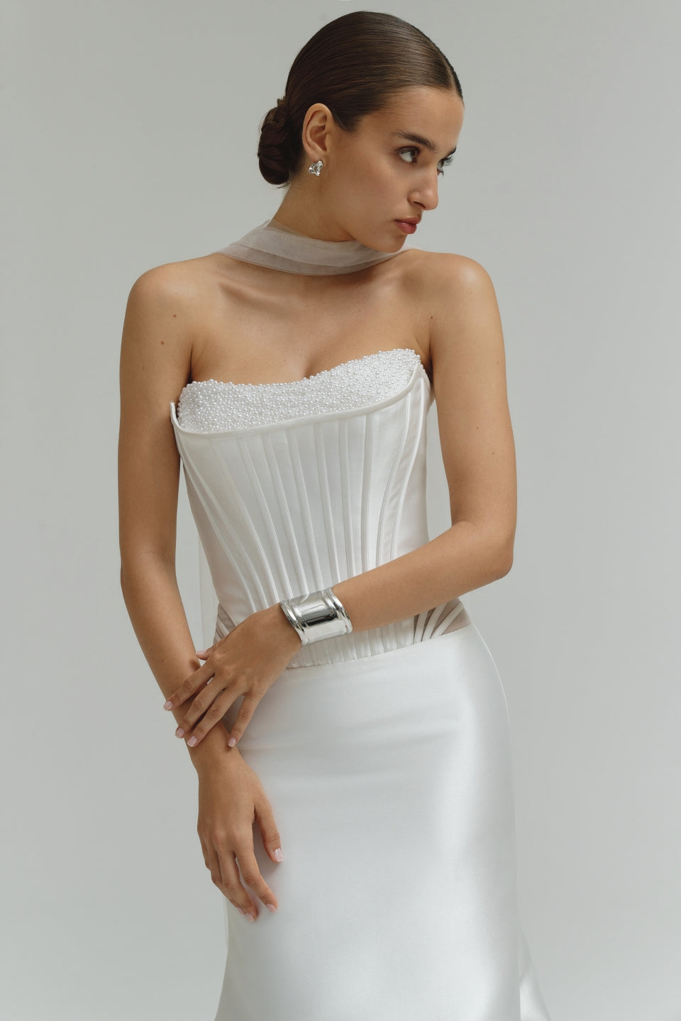 Woman wearing a dropped waist Mikado fitted wedding dress with a textured bodice on a plain background