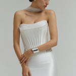 Woman wearing a dropped waist Mikado fitted wedding dress with a textured bodice on a plain background