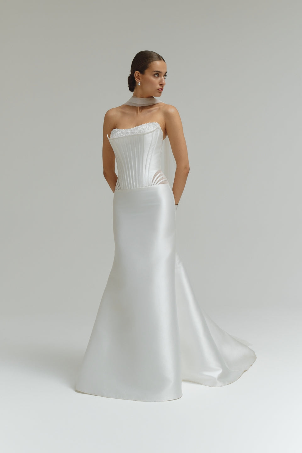 Woman wearing a dropped waist Mikado fitted wedding dress on a plain background