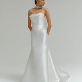 Woman wearing a dropped waist Mikado fitted wedding dress on a plain background