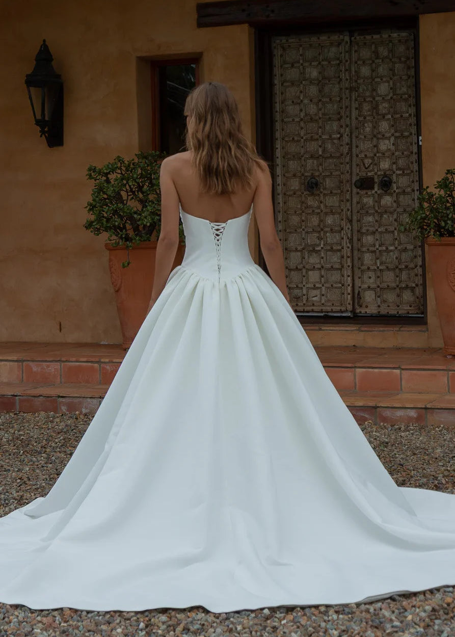 Woman in a Satin A-Line Wedding Dress standing in front of a rustic building with a wooden door.