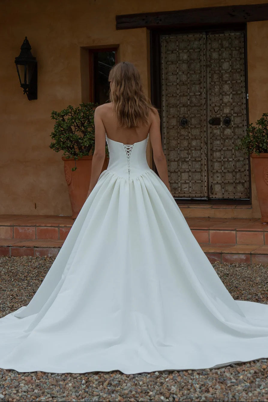 Woman in a Satin A-Line Wedding Dress standing in front of a rustic building with a wooden door.