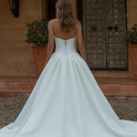Woman in a Satin A-Line Wedding Dress standing in front of a rustic building with a wooden door.