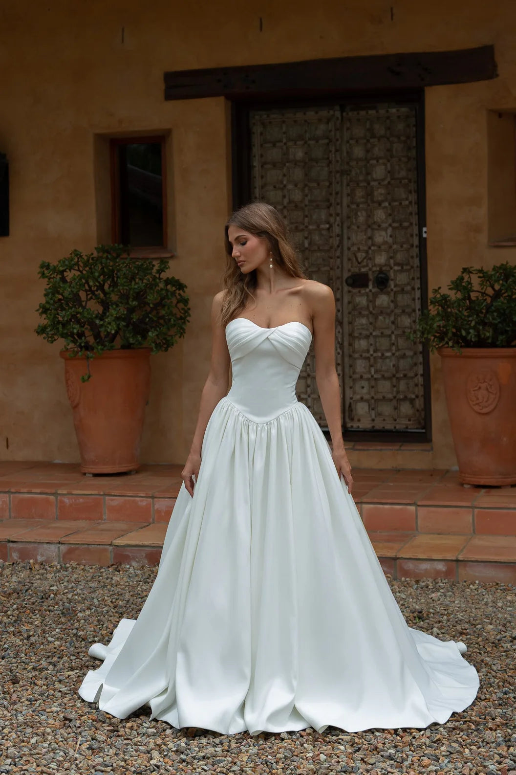 Woman in a Satin A-Line Wedding Dress standing in front of a rustic building.