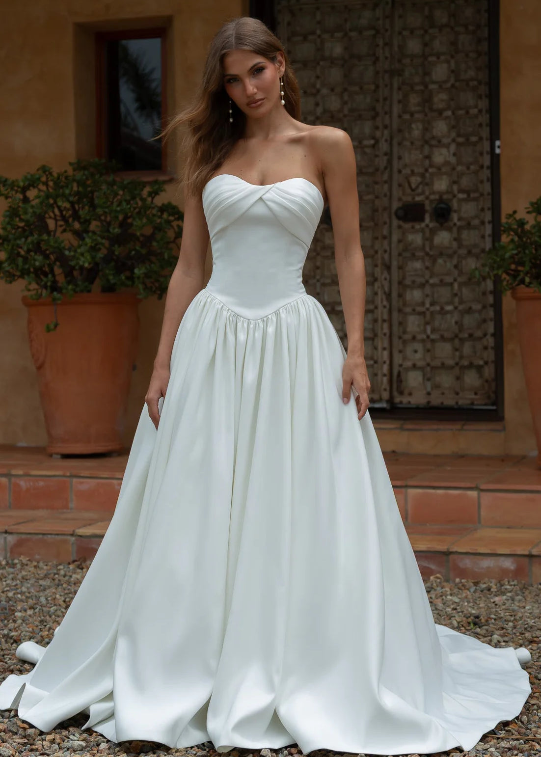 Woman wearing a Satin A-Line Wedding Dress standing outdoors with a rustic background.