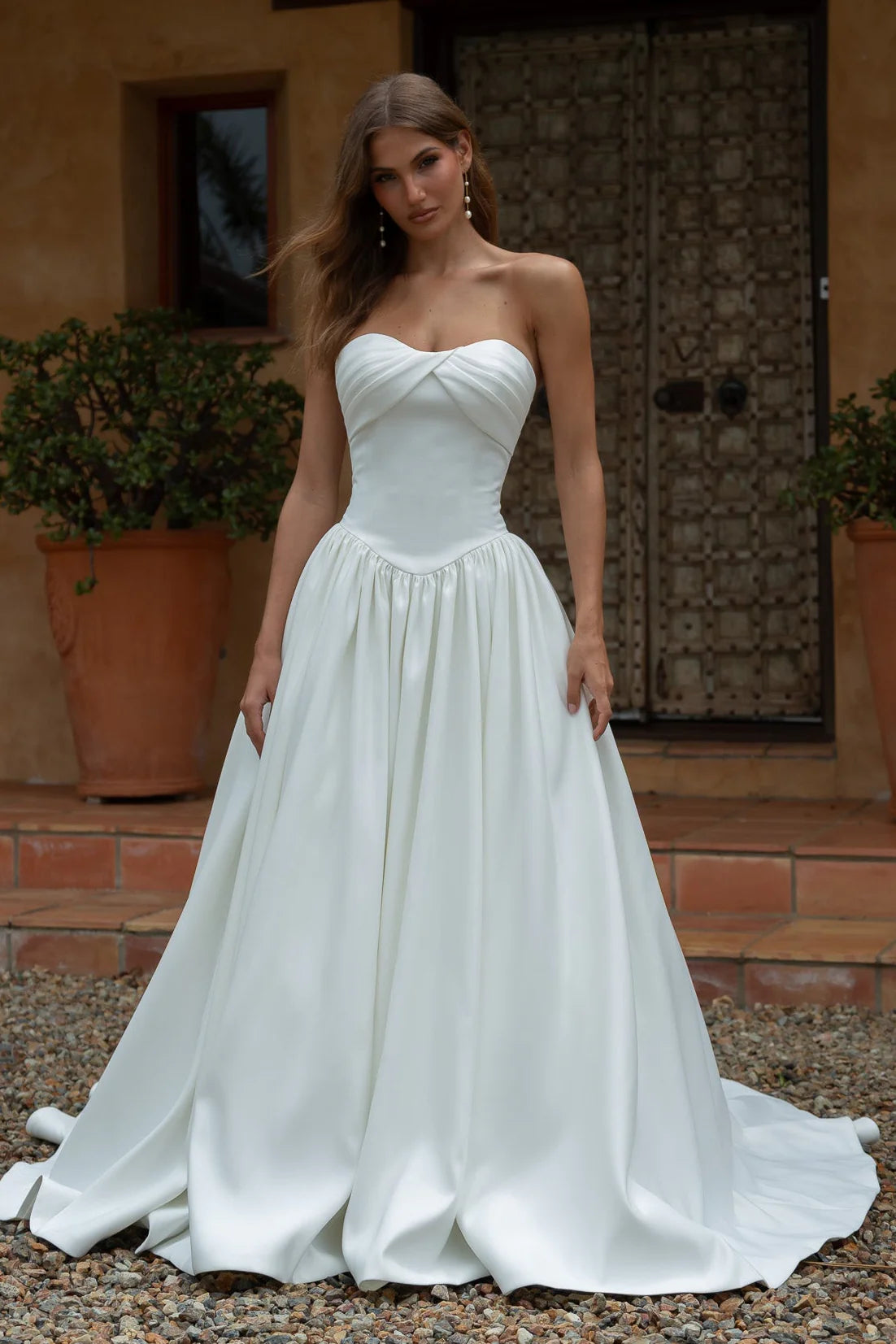Woman wearing a Satin A-Line Wedding Dress standing outdoors with a rustic background.