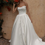 Woman in a Mikado A-Line Wedding Dress standing against a textured wall with red flowers.