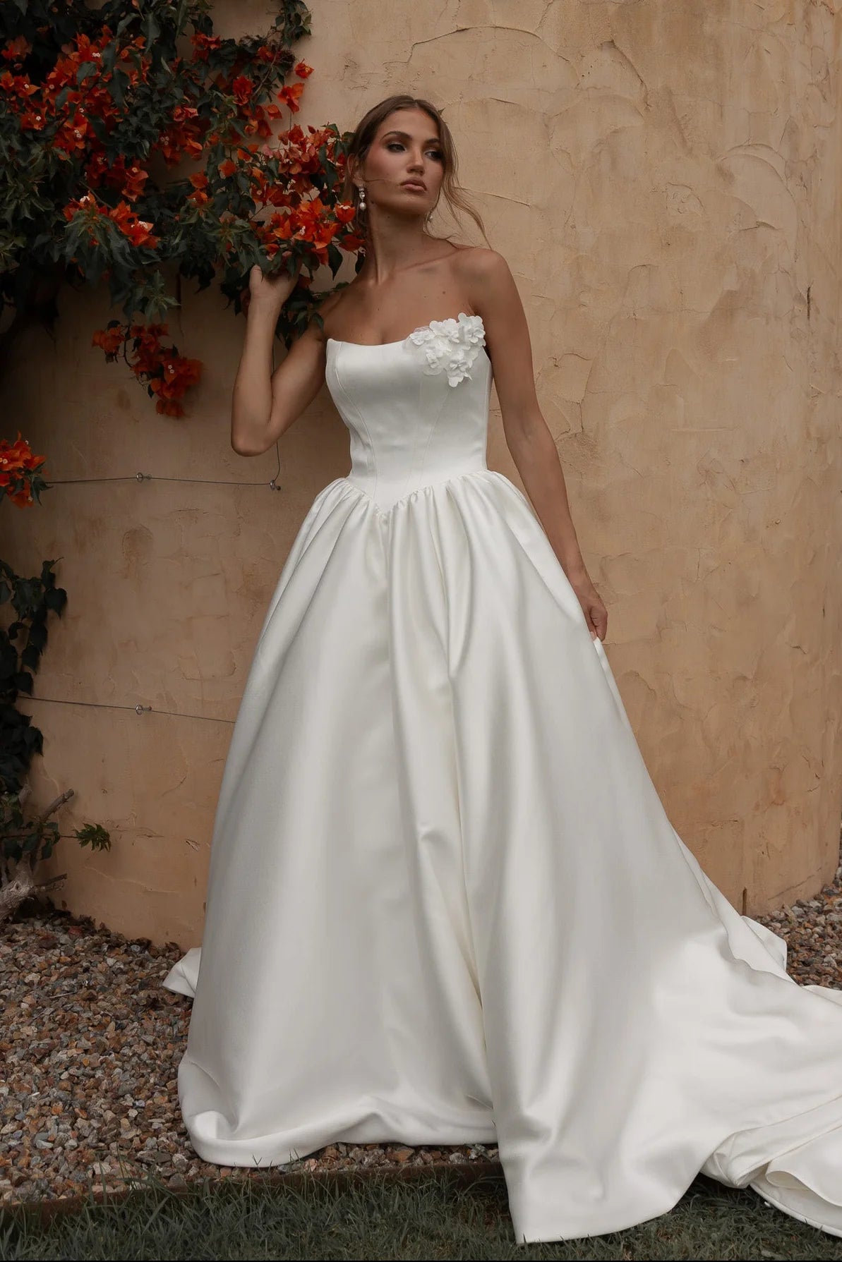Woman in a Mikado A-Line Wedding Dress standing against a textured wall with red flowers.