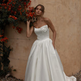 Woman in a Mikado A-Line Wedding Dress standing against a beige wall with red flowers.