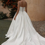 White wedding dress with a lace-up back being worn by a woman outdoors.