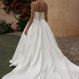 White wedding dress with a lace-up back being worn by a woman outdoors.