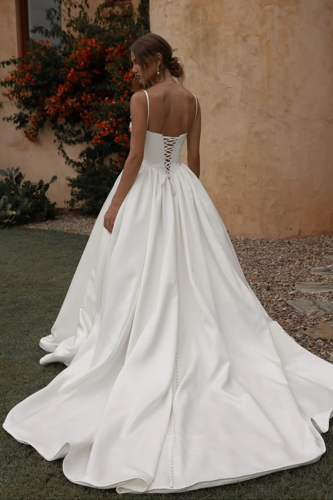 White wedding dress with a lace-up back being worn by a woman outdoors.