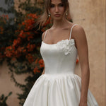 Woman in a Mikado A-Line Wedding Dress standing outdoors with a building and plants in the background