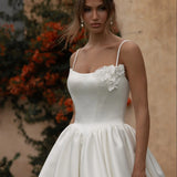 Woman in a Mikado A-Line Wedding Dress standing outdoors with a building and plants in the background