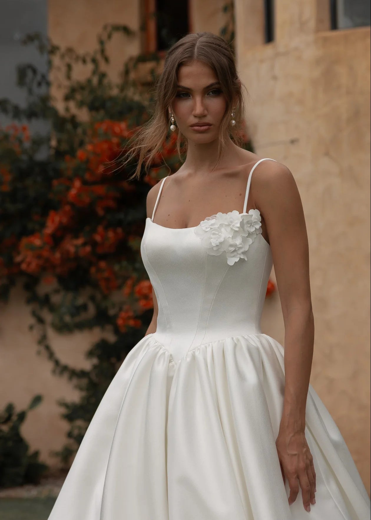 Woman in a Mikado A-Line Wedding Dress standing outdoors with a building and plants in the background