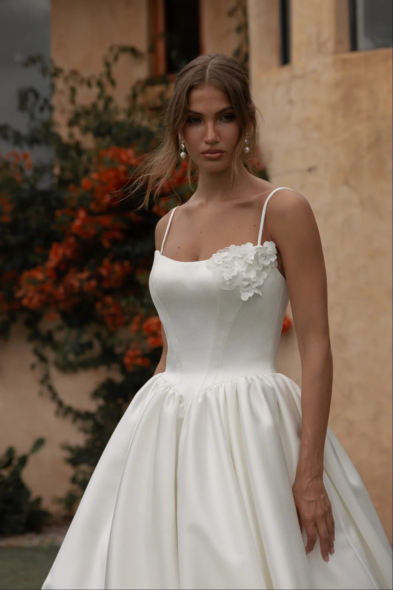 Woman in a Mikado A-Line Wedding Dress standing outdoors with a building and plants in the background