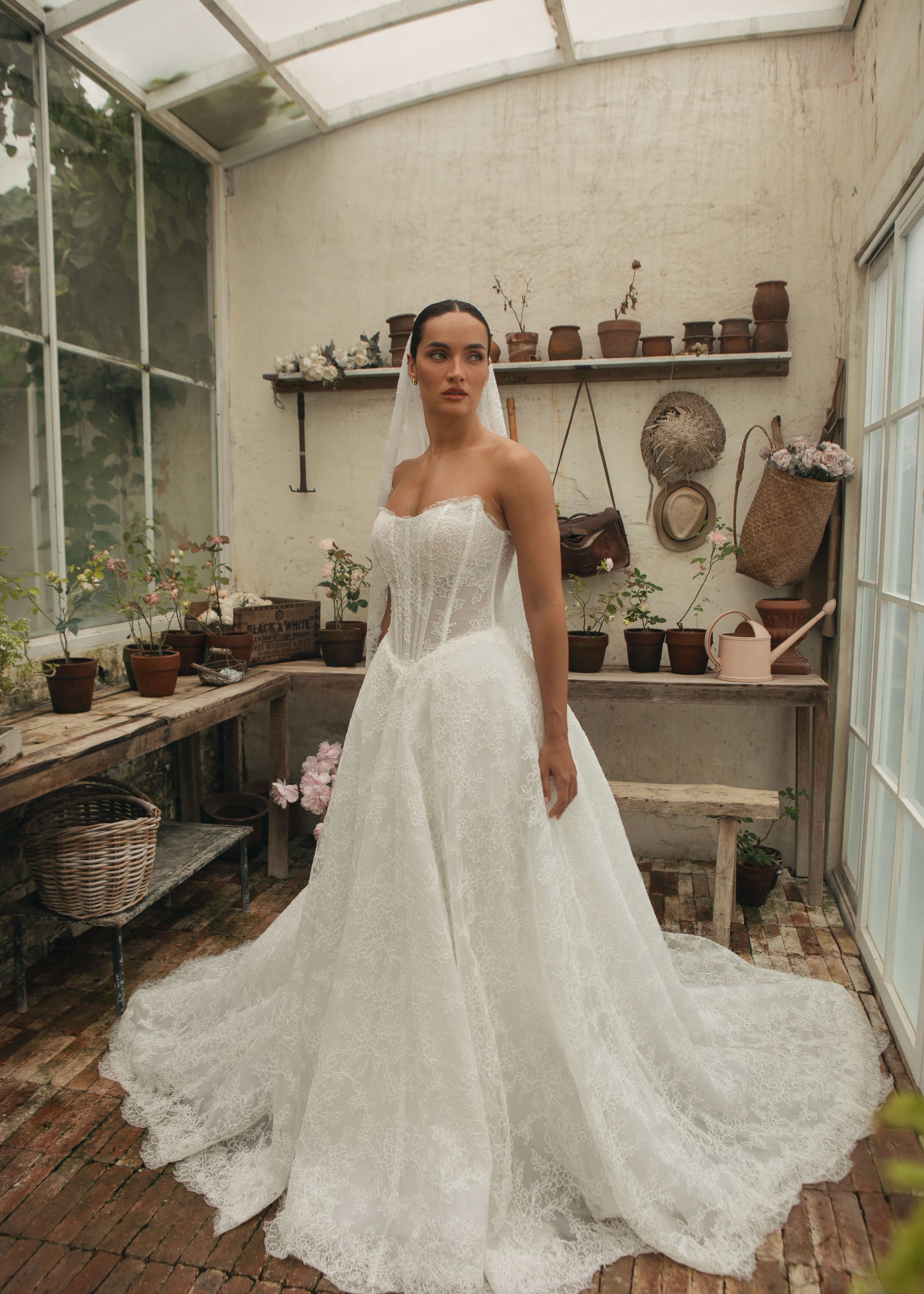 Woman in a Lace A-Line Wedding Dress standing in a greenhouse with plants and shelves.