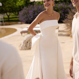 Woman in Genesis wedding dress by Modeca standing outdoors with greenery and a white umbrella in the background.