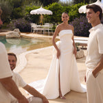 Woman in Genesis wedding dress by Modeca standing by a pool with two men, all smiling.