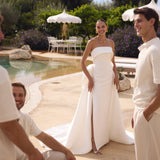 Woman in Genesis wedding dress by Modeca standing by a pool with two men, all smiling.