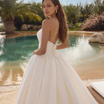 Woman in Ghada wedding dress by Modeca standing by a pool with palm trees in the background