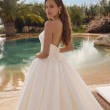 Woman in Ghada wedding dress by Modeca standing by a pool with palm trees in the background