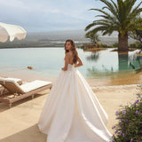 Woman in Ghada wedding dress by Modeca standing by a pool with palm trees and a clear sky.