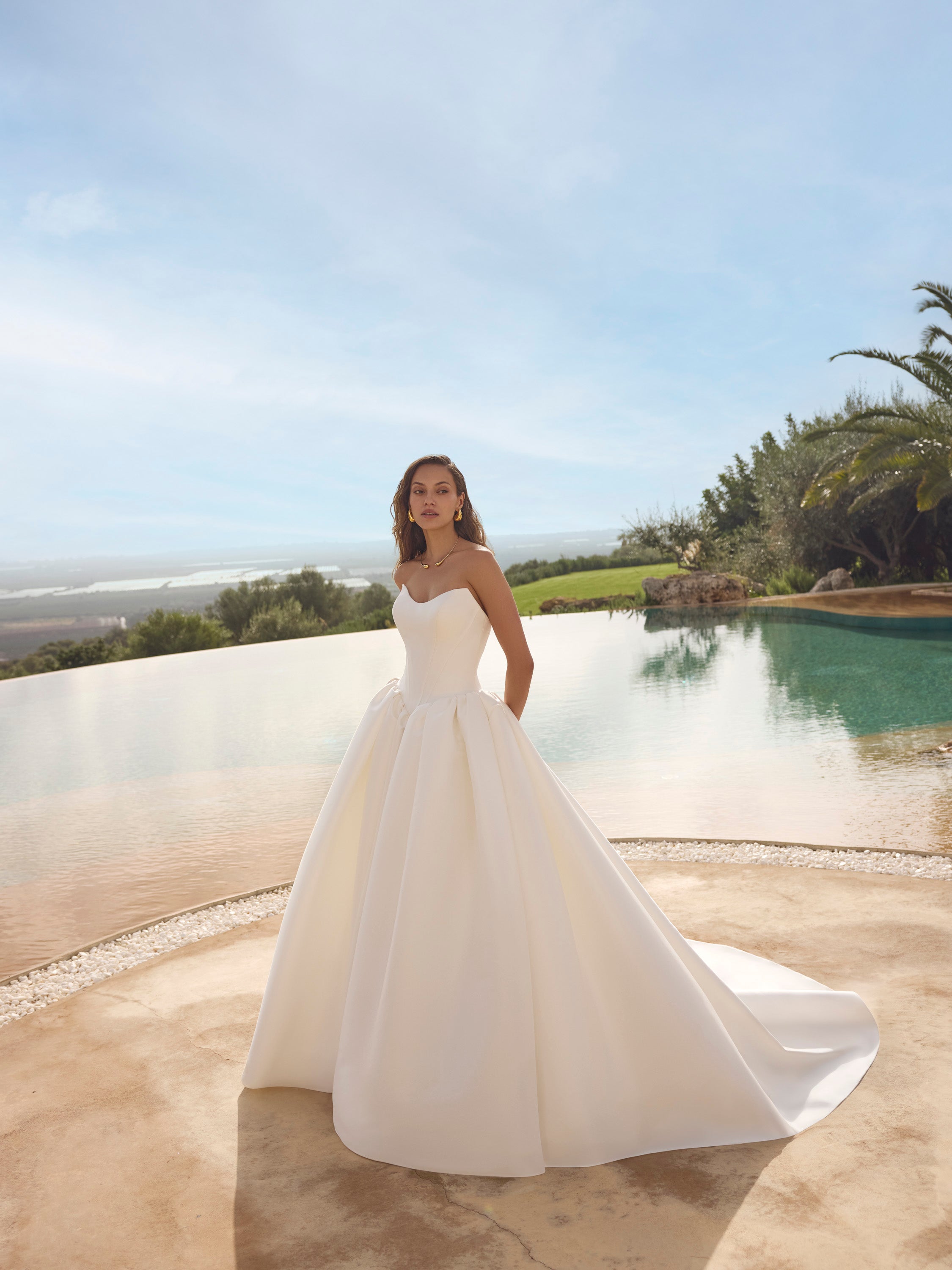 Woman in Ghada wedding dress by Modeca standing by a pool with a scenic background