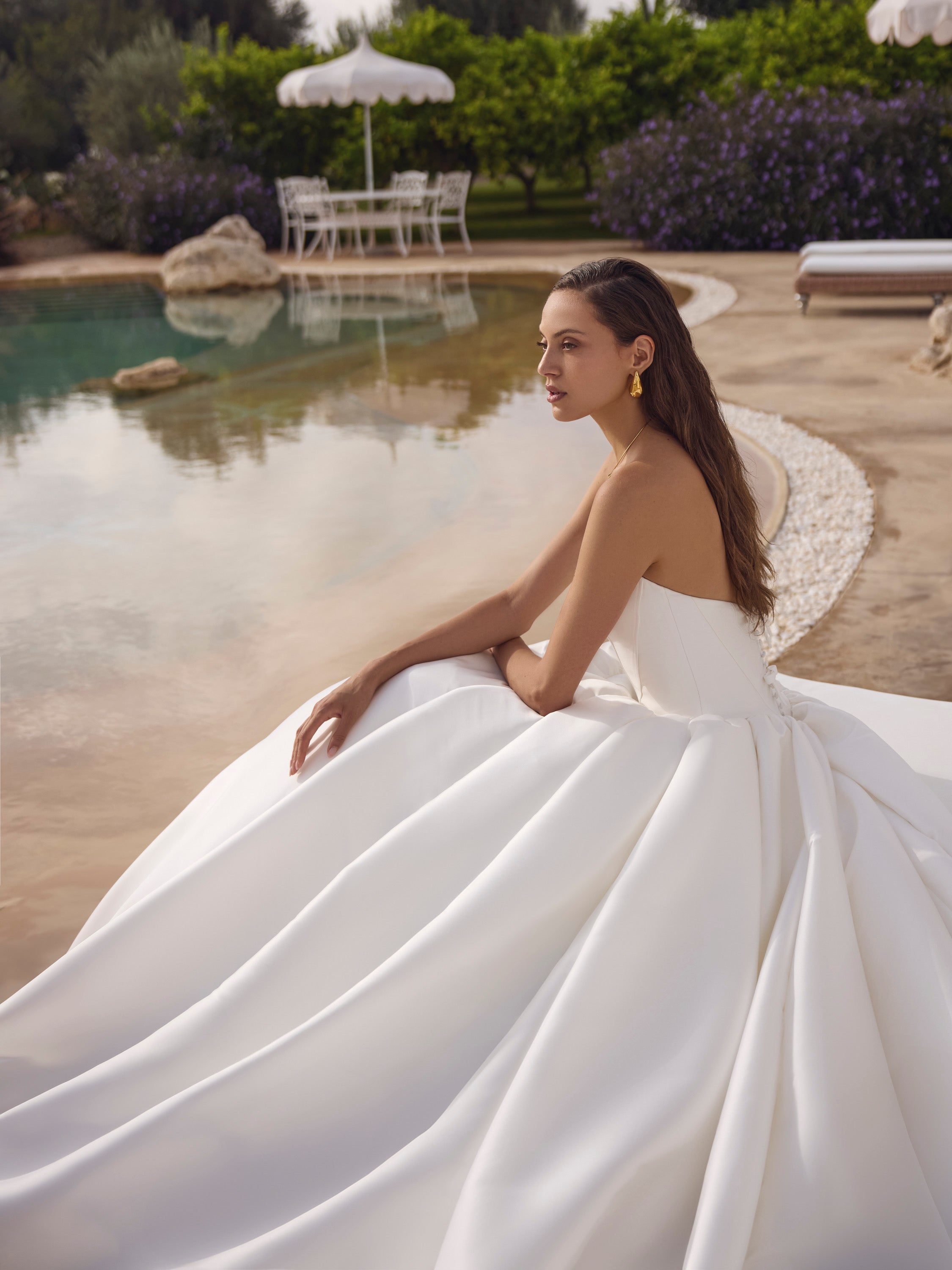 Woman in a white wedding dress sitting by a pool with a scenic background