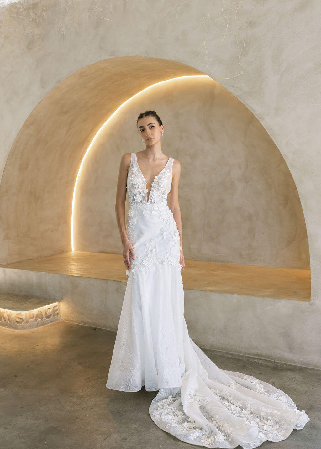 Woman in a Floral Fit and Flare Bridal Gown standing in a modern architectural setting with arches.