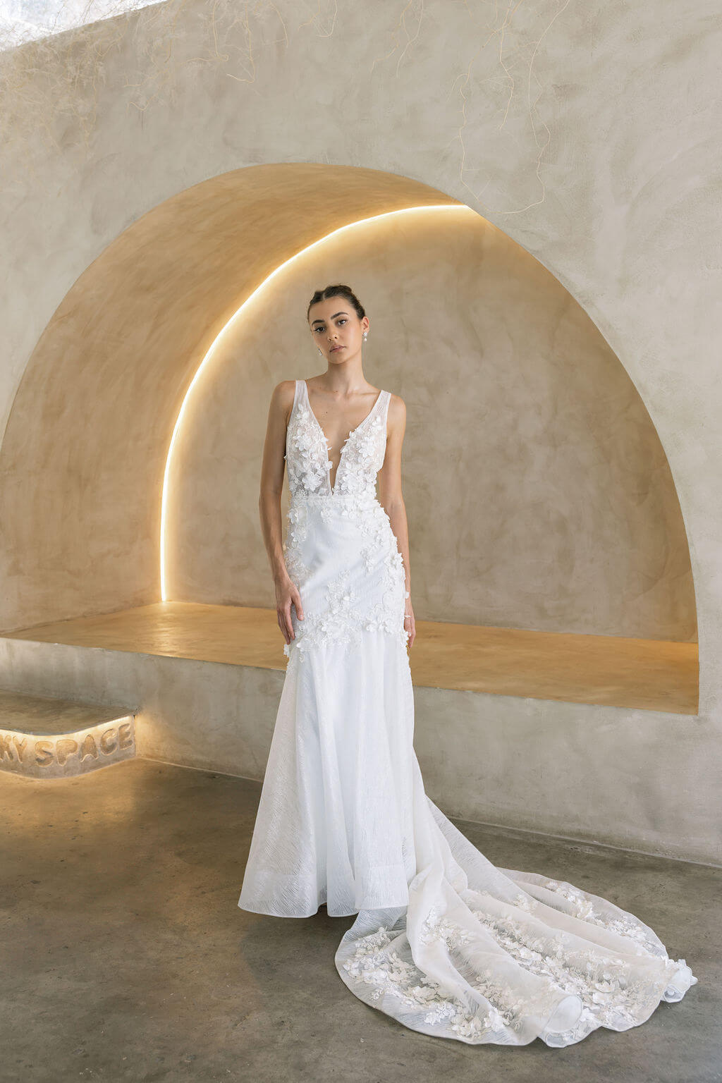 Woman in a Floral Fit and Flare Bridal Gown standing in a modern architectural setting with arches.