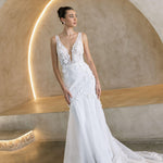 Woman in a Floral Fit and Flare Bridal Gown standing against a textured wall with architectural elements.