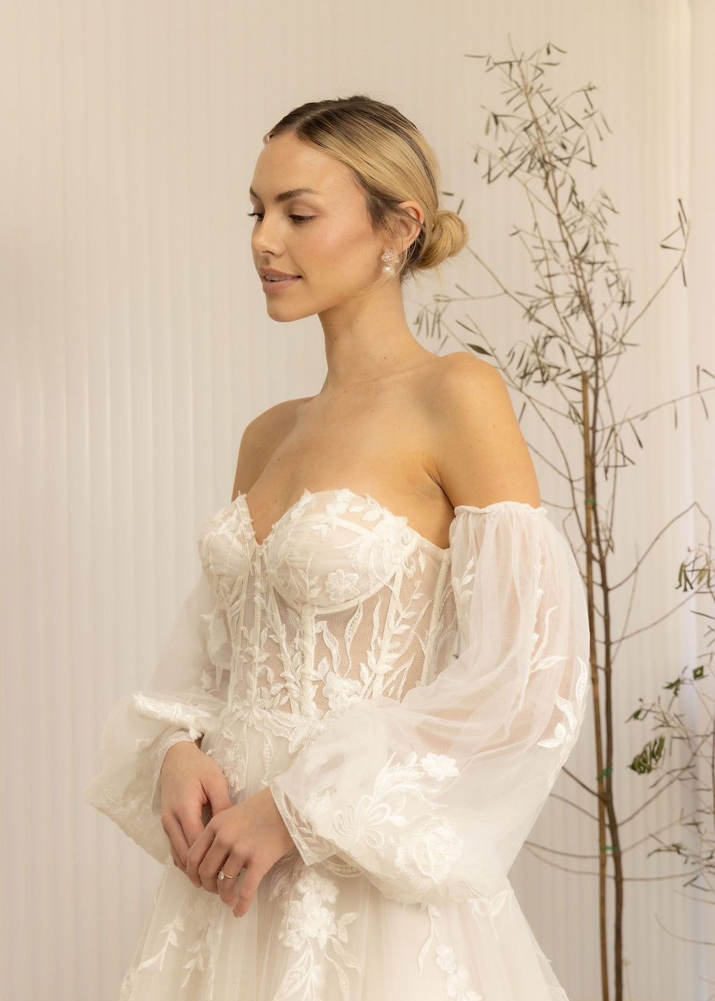 Woman wearing a white Romantic Lace Wedding Dress with long sleeves in a softly lit room.