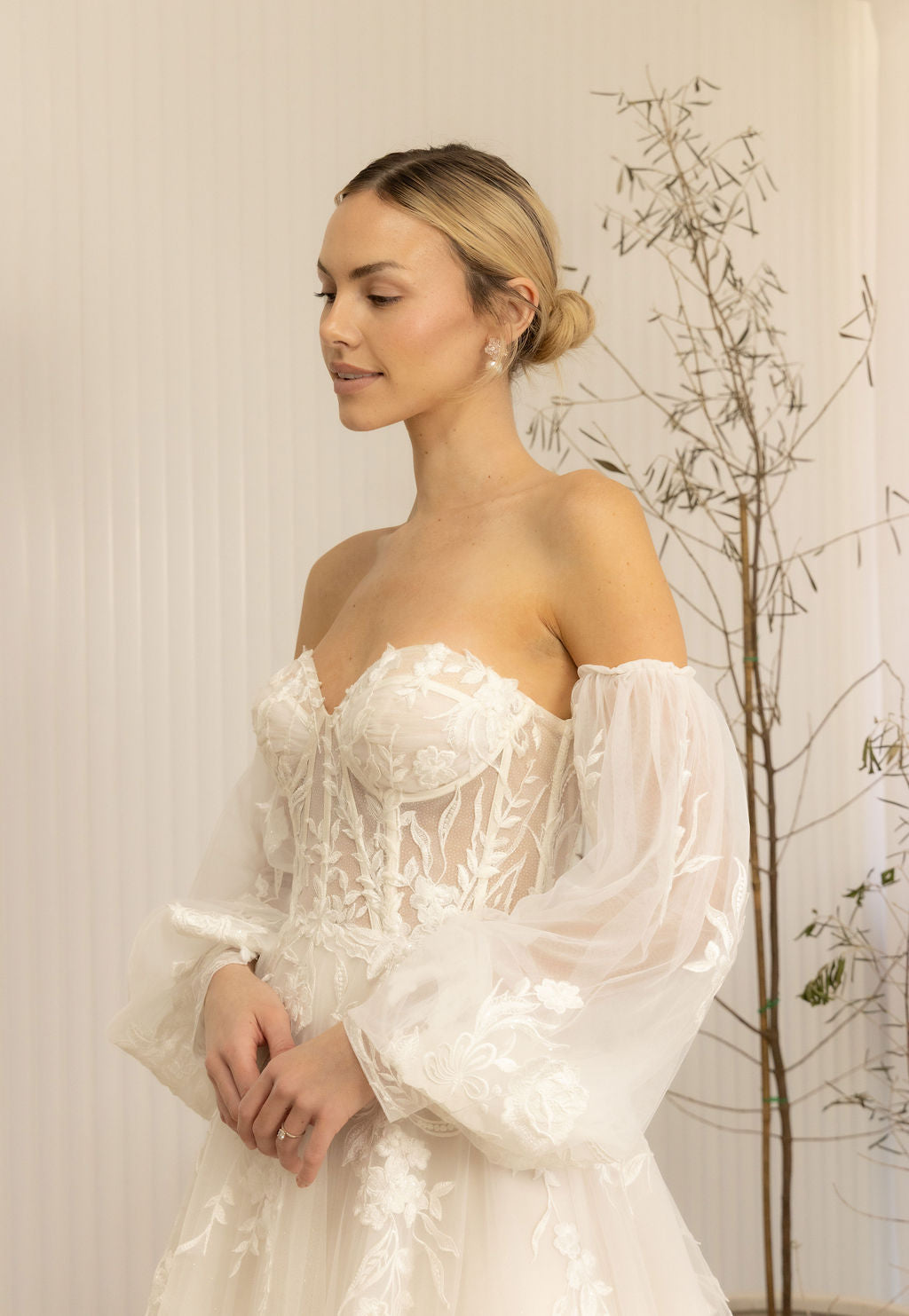 Woman wearing a white Romantic Lace Wedding Dress with long sleeves in a softly lit room.