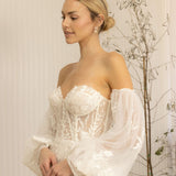 Woman wearing a white Romantic Lace Wedding Dress with long sleeves in a softly lit room.
