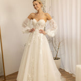 Woman wearing a white Romantic Lace Wedding Dress in a room with curtains and a plant.