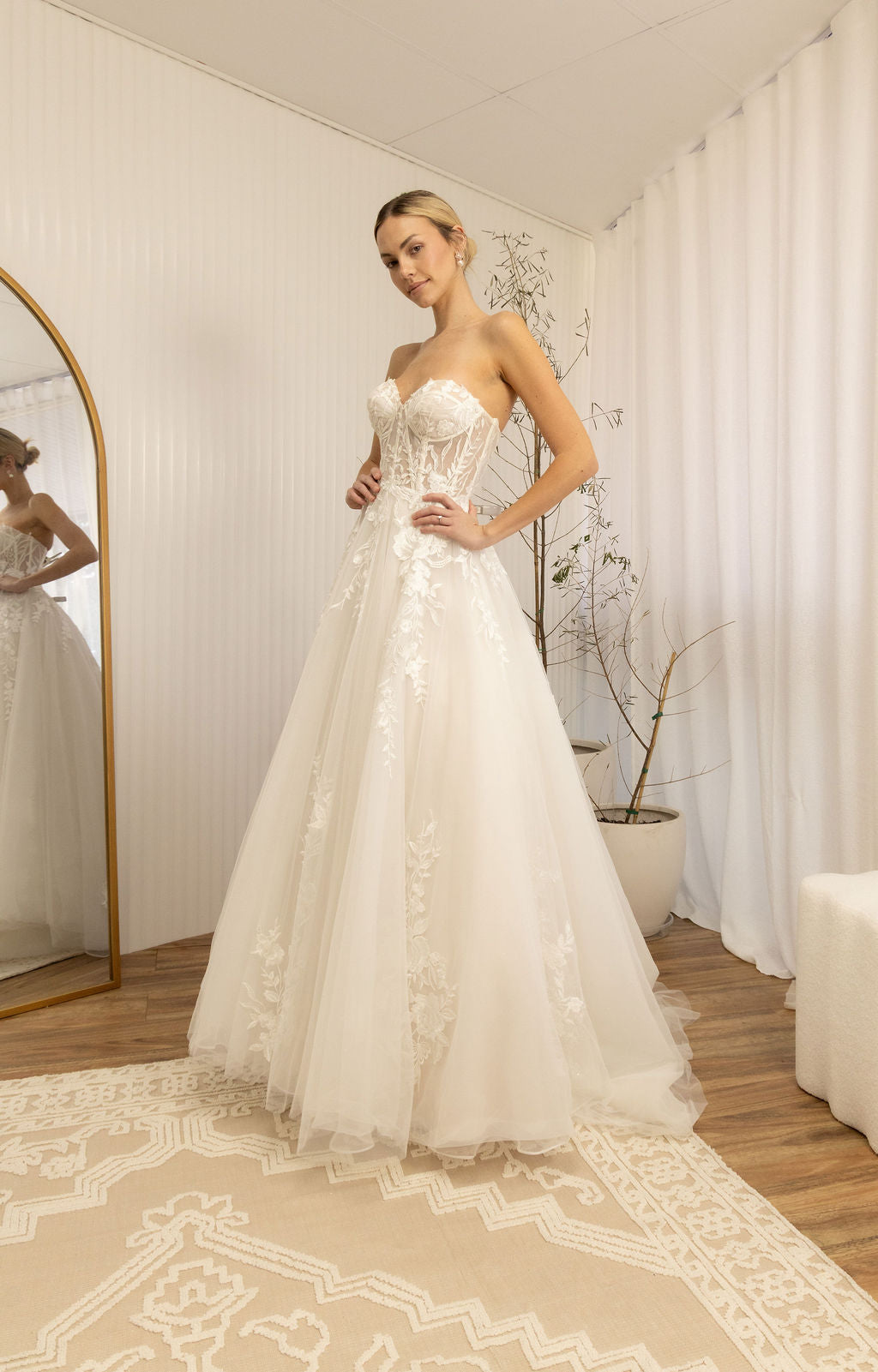 Woman trying on a Romantic Lace Wedding Dress in a room with a mirror and decor.