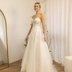 Woman in a white Romantic Lace Wedding Dress standing in a room with white walls and a white curtain.