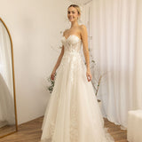 Woman in a white Romantic Lace Wedding Dress standing in a room with white walls and a white curtain.